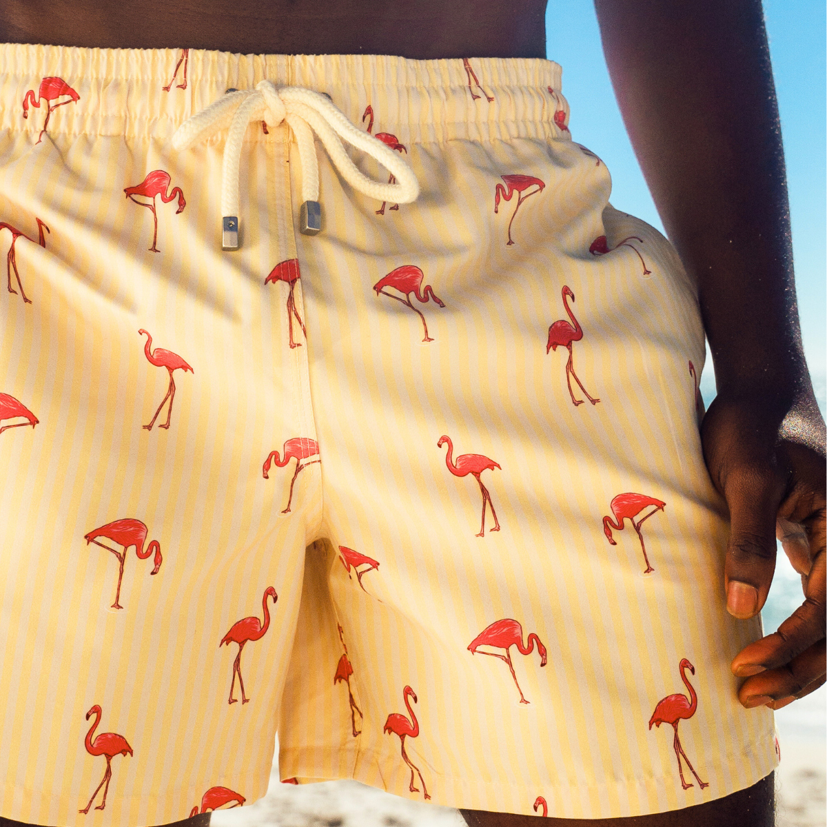 Yellow shorts with pink flamingo pattern worn by a person on a beach.